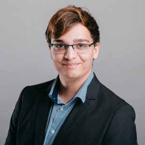 jeune homme en costume noir souriant avec des lunettes